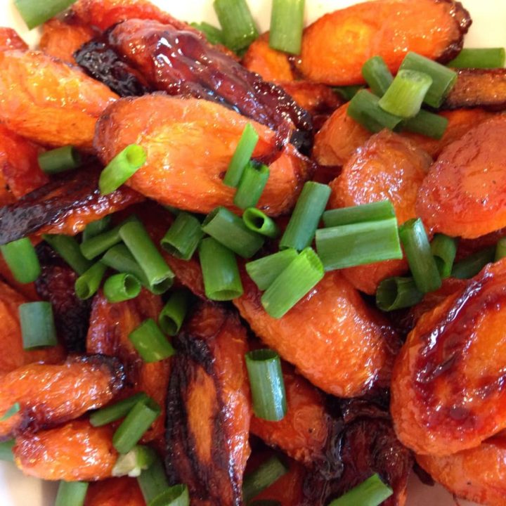 A close up of roasted carrots topped with sliced green onions.