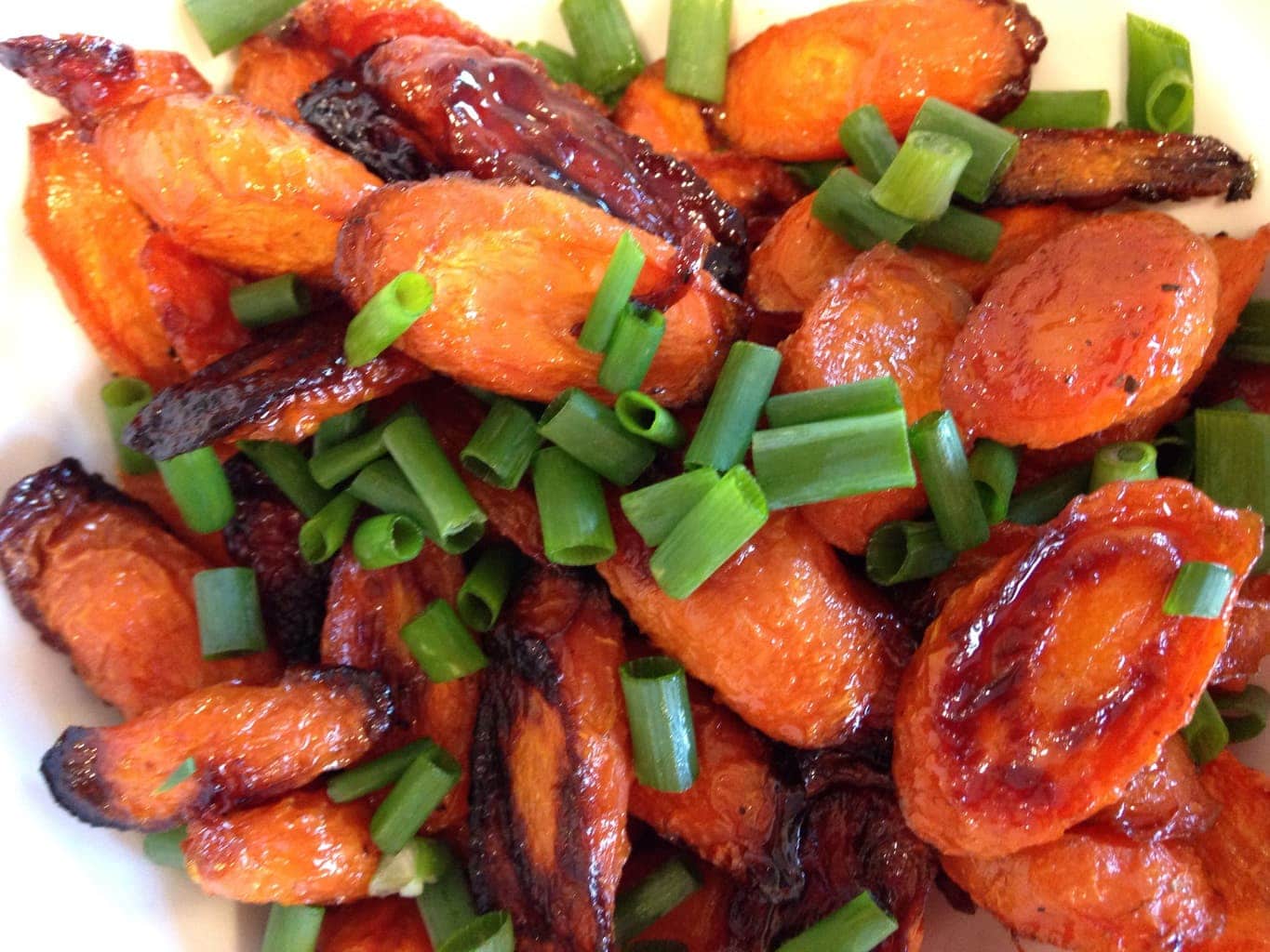 A close up of roasted carrots topped with sliced green onions.