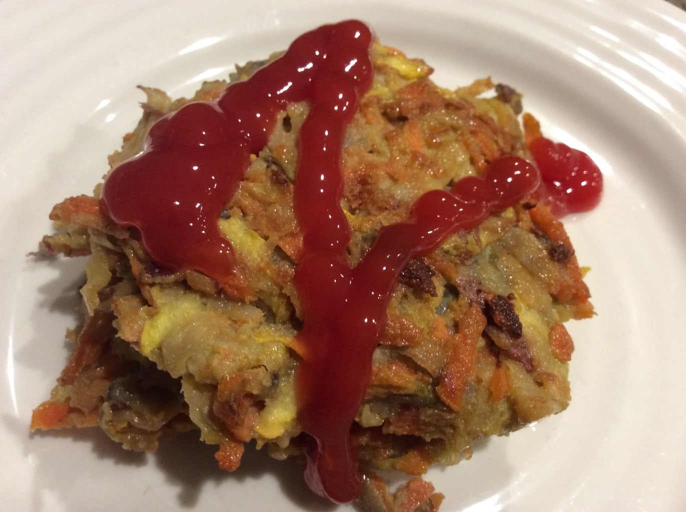 Veggie pancakes on a white plate and drizzled with ketchup. 