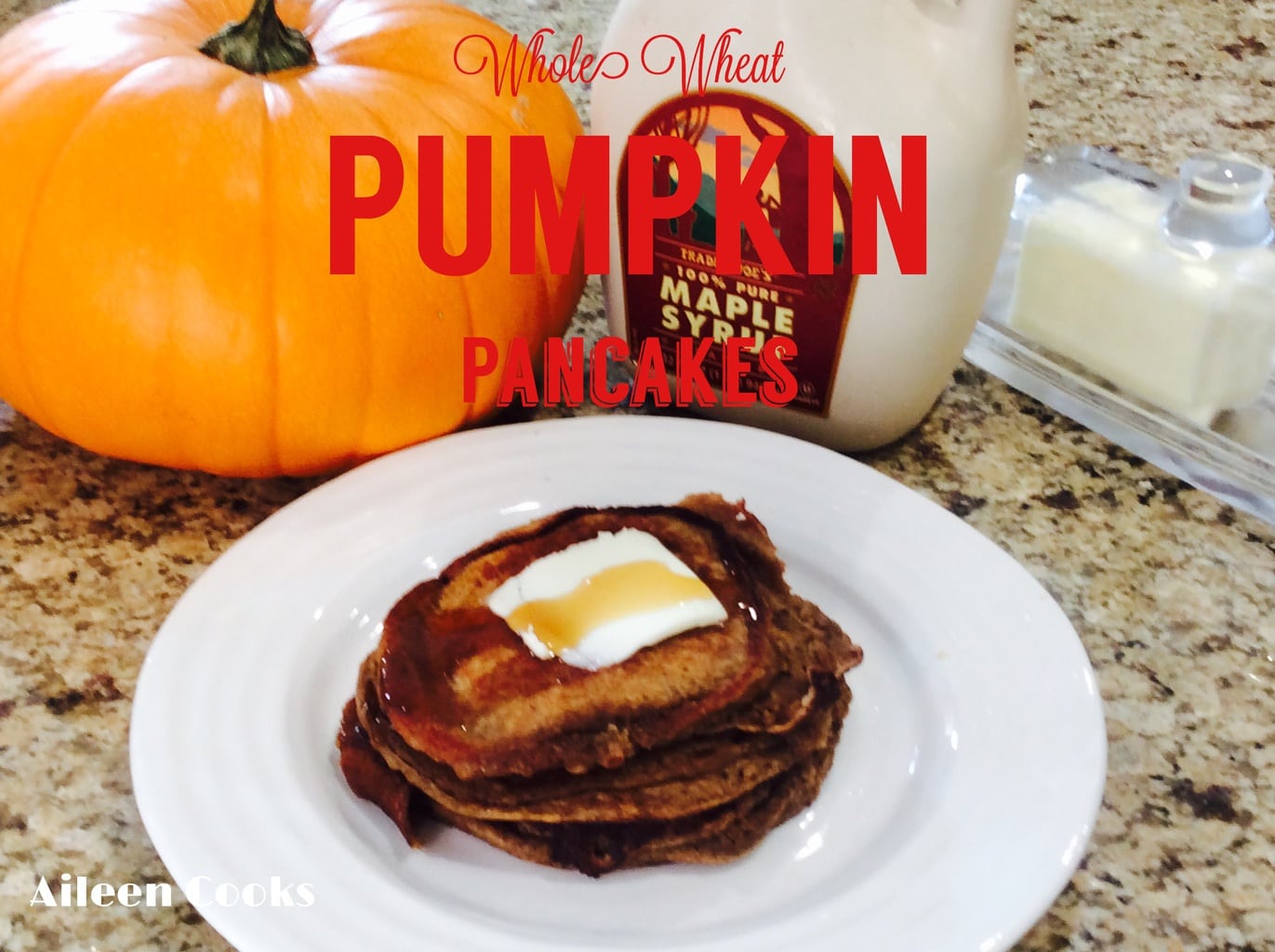 A stack of whole wheat pumpkin pancakes next to a pumpkin, bottle of maple syrup, and butter dish.