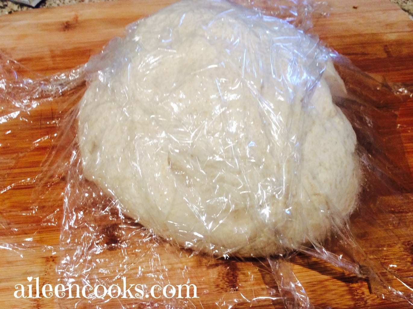 A ball of whole wheat french bread dough under plastic wrap.
