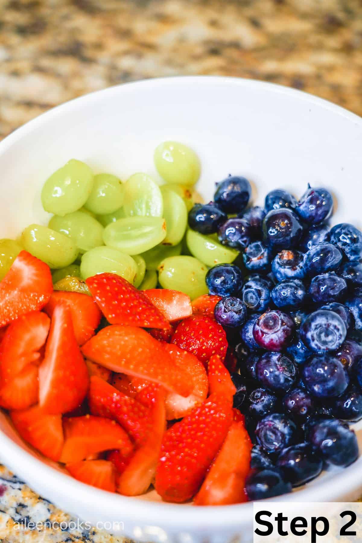 A large white bowl filled with strawberries, green grapes, and blueberries.