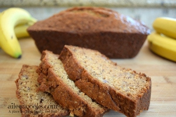 Three slices of banana bread in front of a loaf of banana bread.