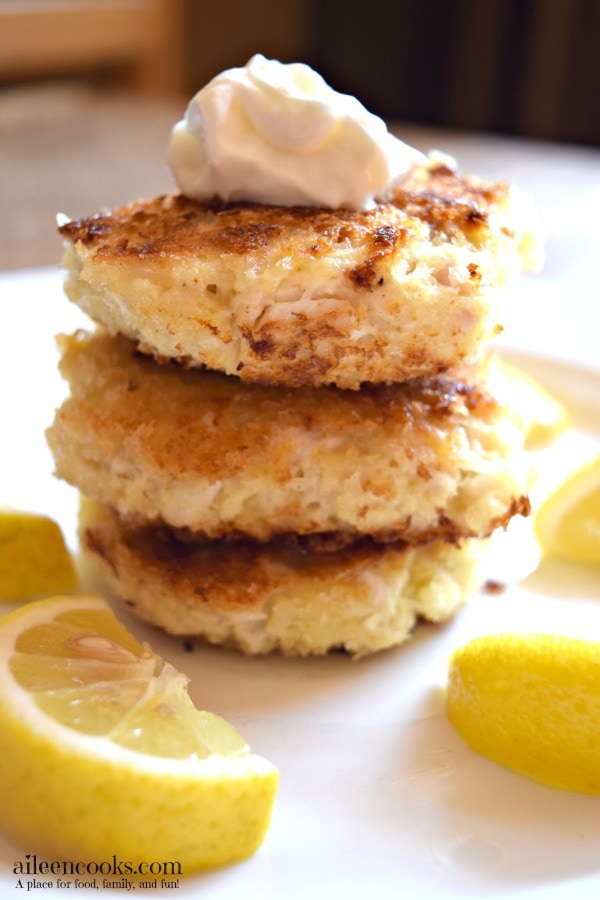 Tilapia fish cakes stacked up on a white plate and topped with sour cream.