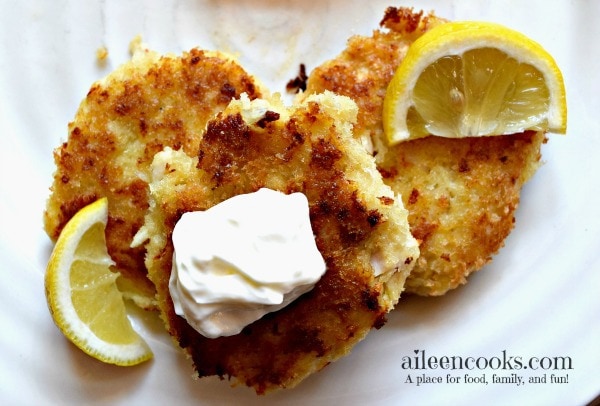 Three tilapia cakes topped with sour cream and lemon wedges.