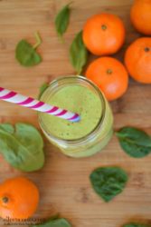 Mandarin Orange Spinach Smoothie on a wooden cutting board with striped straw.