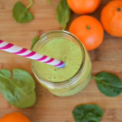 Mandarin Orange Spinach Smoothie on a wooden cutting board with striped straw.