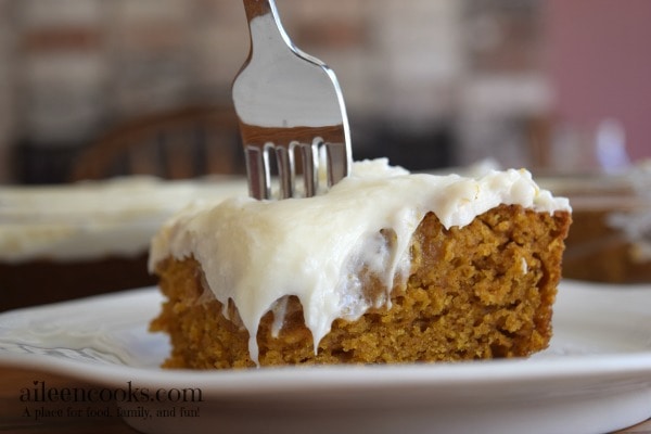 A slice of pumpkin sheet cake with cream cheese frosting with the fork sticking out of the top of the cake.