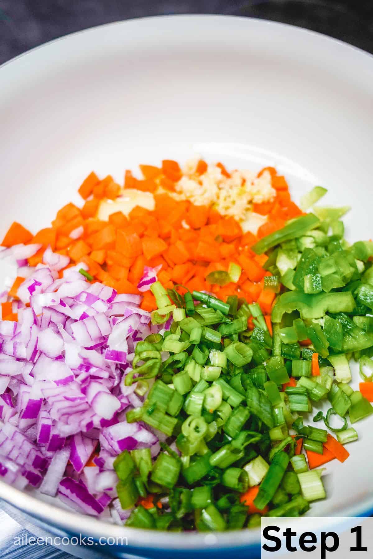 A large skillet filled with diced green onion, red onion, carrot, and garlic.