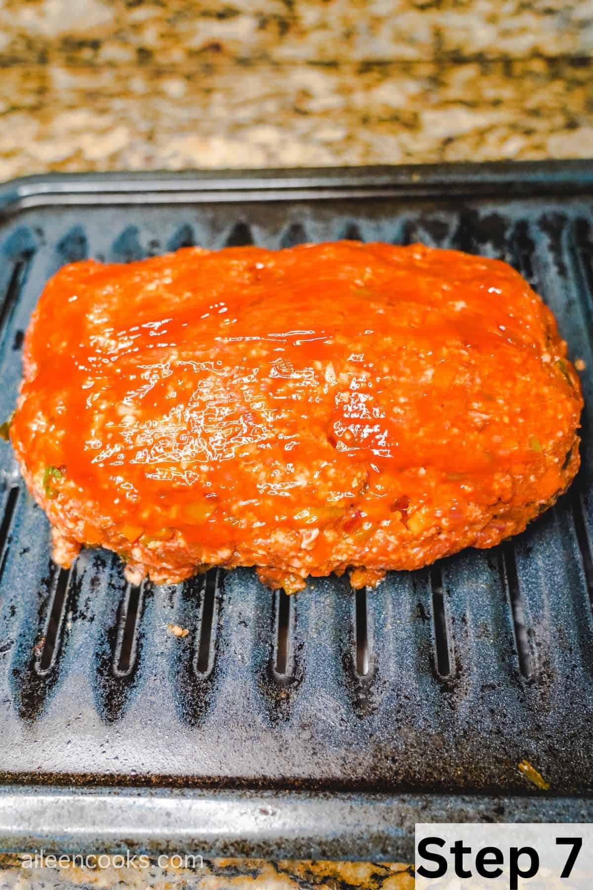 A shaped meatloaf coated in a ketchup glaze, on top of a broiler pan.
