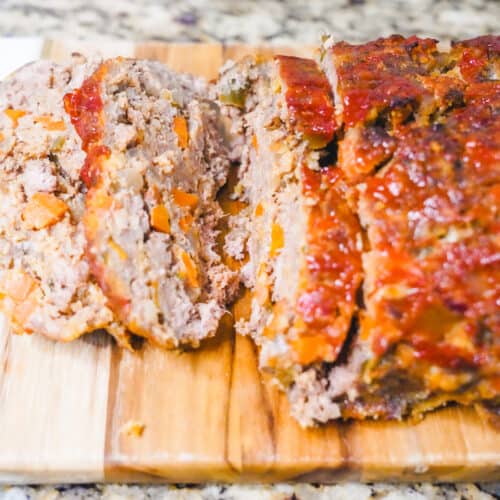 A meatloaf sliced up on a wooden cutting board.