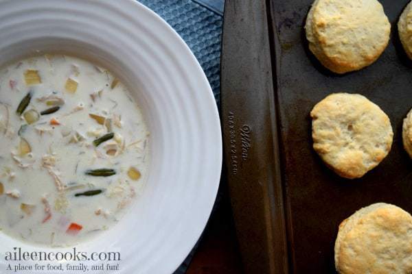 Overhead shot of large bowl filled with creamy chicken pot pie soup next to a batch of biscuits.