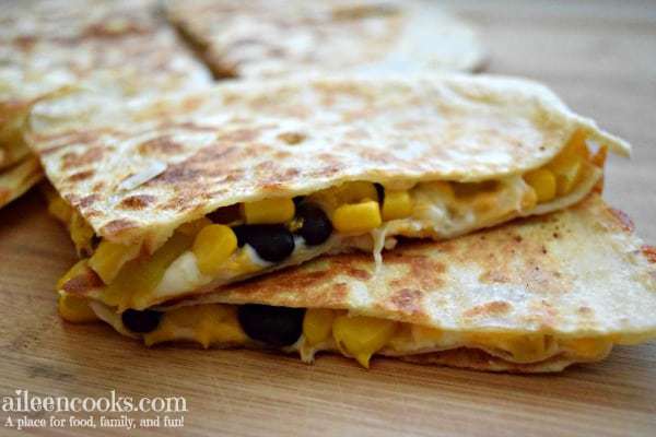 Corn and black bean quesadillas cut into triangles and stacked on a wooden cutting board.