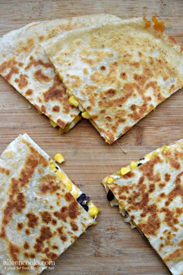 Black bean and corn quesadillas on a wooden cutting board with a few pieces of corn falling out.