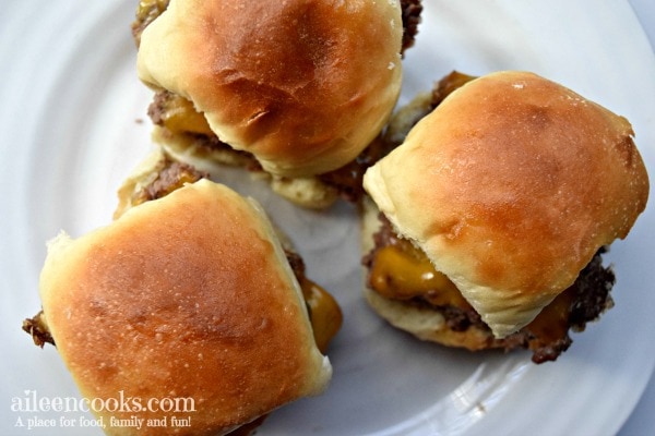 A white plate with three easy cheeseburger sliders topped with browned rolls.