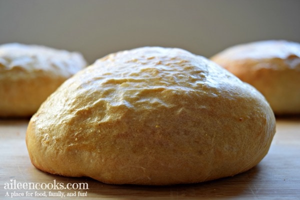 An italian bread bowl on a cutting board with two more of the Italian bread bowls recipe in the background.