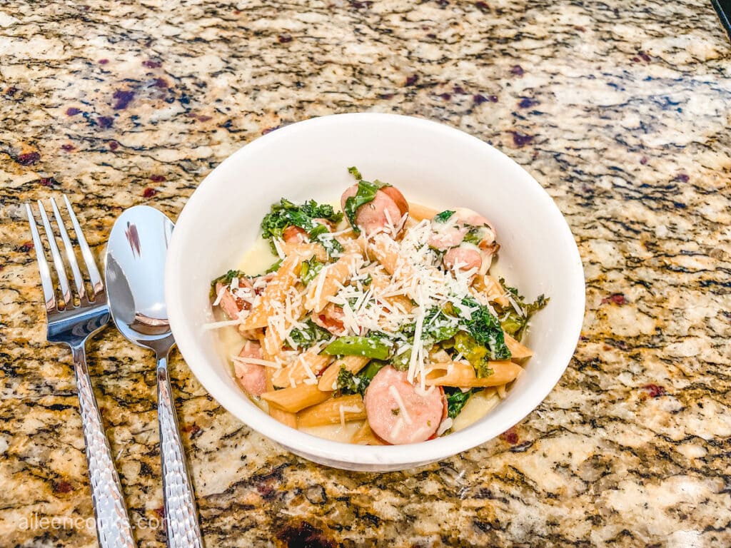 A bowl of smoked sausage and kale pasta in a white bowl.