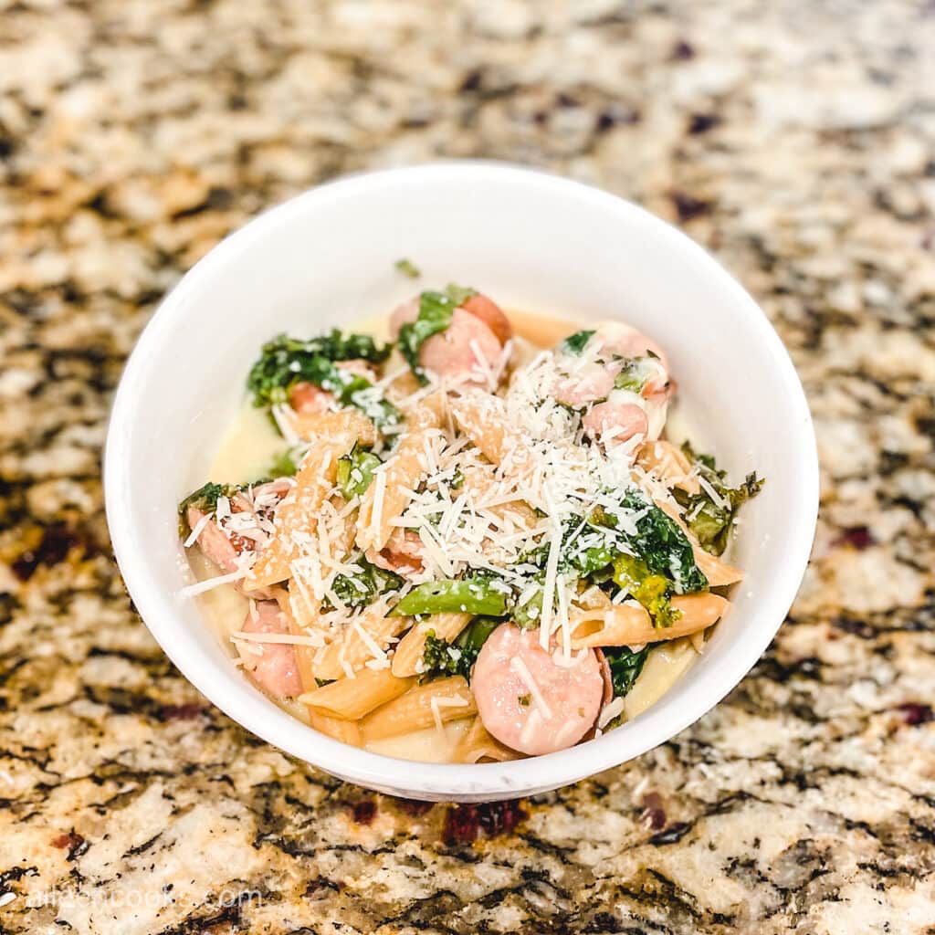 A bowl of pasta with kale and sliced sausages, topped with parmesan cheese.