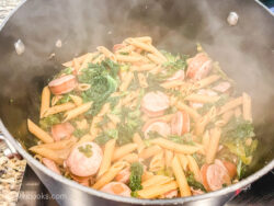 A pot of steaming pasta, kale, and sausage.