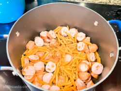 A pot of sliced smoked sausages and penne pasta, covered in chicken broth.