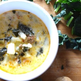 A white soup bowl filled with olive Garden zuppa toscana on top of a wooden cutting board.