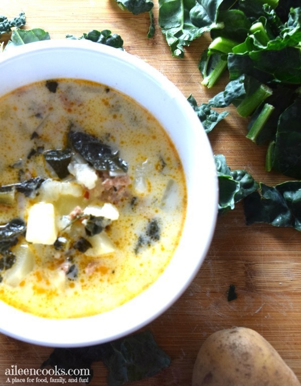 A white soup bowl filled with olive Garden zuppa toscana on top of a wooden cutting board.