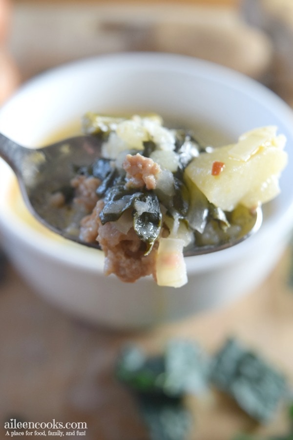 A spoonful of instant pot zuppa toscana held over a white bowl filled with the Italian soup.