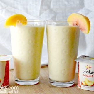 2 glasses of smoothie with slices of peaches on the glass and two containers of Yoplait Harvest Peach yogurt.