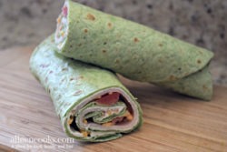 Spinach wrap rolled up with turkey, cheese, and tomatoes peeking out.