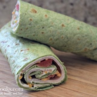 Spinach wrap rolled up with turkey, cheese, and tomatoes peeking out.