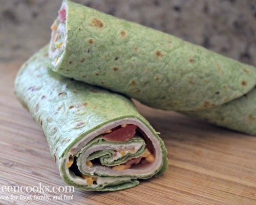 Spinach wrap rolled up with turkey, cheese, and tomatoes peeking out.