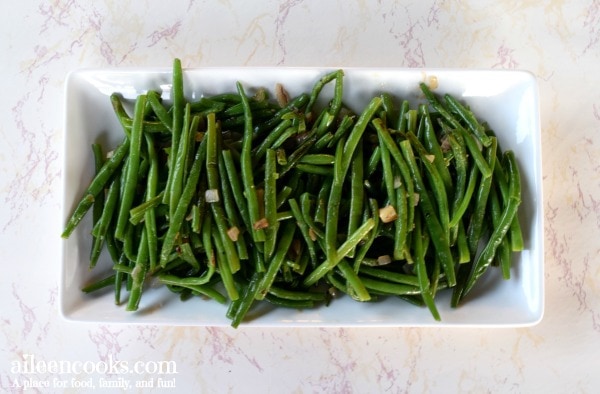 White platter filled with green beans and caramelized shallots