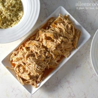 Shredded buffalo chicken on a white platter next to bowl of rice and bowl of corn.