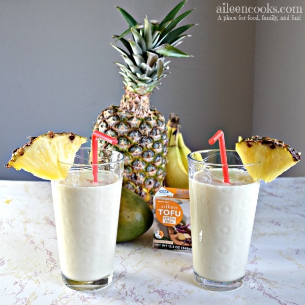 Two protein packed tropical smoothies with pineapple slices and red straws