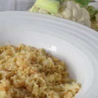 cauliflower rice in a white bowl with whole cauliflower in the background