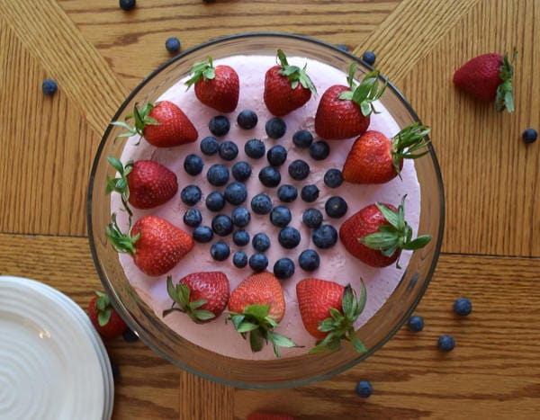 no-bake strawberry cheesecake on glass cake plate and topped with fresh berries.