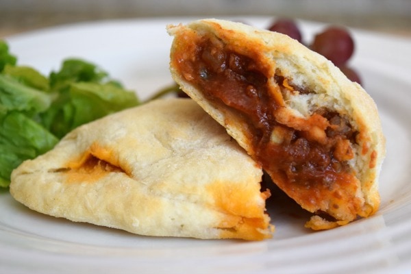 Sloppy joe pocket cut in half to show fillinging on a white plate with green salad and red grapes in the background