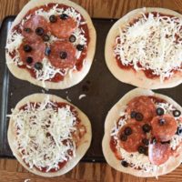 4 homemade freezer pizzas. 2 are plain cheese and 2 are pepperoni and olive, all sitting on top of a large cookie sheet.