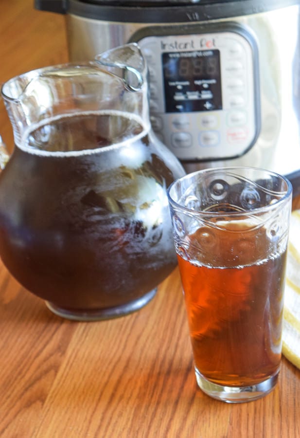 Pitcher of iced tea and glass of iced tea set in front of instant pot electric pressure cooker on a wood surface.