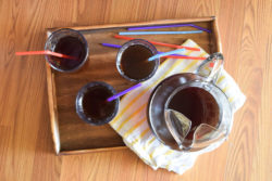 Overhead shot of wood tray holding piture of instant pot iced tea, 3 glasses of iced tea, colorful straws, and yellow striped towel.
