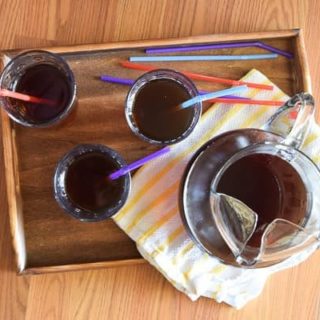 Overhead shot of wood tray holding piture of instant pot iced tea, 3 glasses of iced tea, colorful straws, and yellow striped towel.