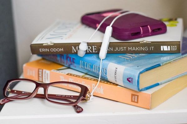 Stack of books, glasses, and phone on a nightstand.