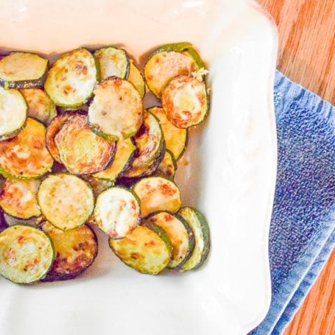 Parmesan zucchini rounds in rectangular baking dish over folded blue dish towel.