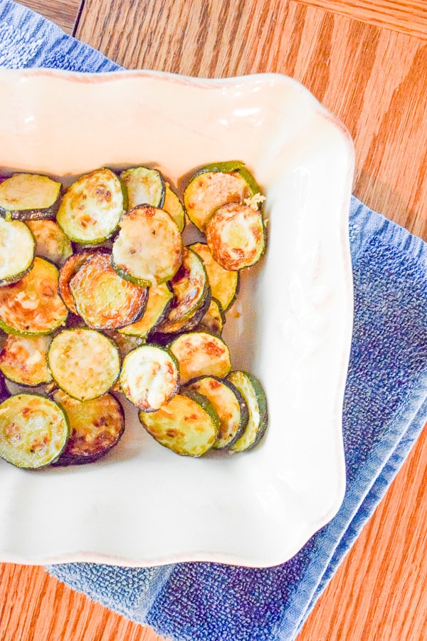 Parmesan zucchini rounds in rectangular baking dish over folded blue dish towel.