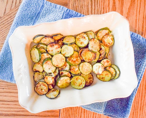 Overhead shot of baking dish filled with parmesan zucchini rounds sitting on top of a folded blue dish towel.