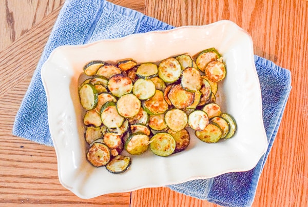 Overhead shot of baking dish filled with parmesan zucchini rounds sitting on top of a folded blue dish towel.