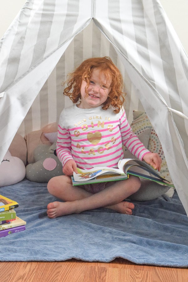 Little girl reading a book in her kids reading nook