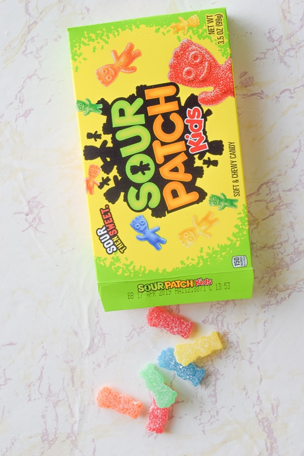 Sour patch kids spilling out of box on marble counter top.