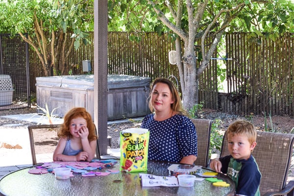 Two kids (girl and boy) sitting outside at a table with their mom, enjoying crafts and Sour Patch Kids.