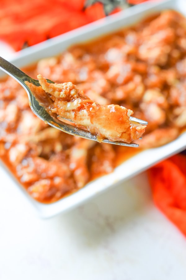 Fork holding a bite of instant pot hawaiian chicken in front of a platter full of the chicken.